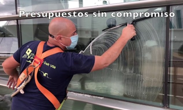 Hombre limpiando una ventana con un paño, usando mascarilla y cinturón de herramientas.